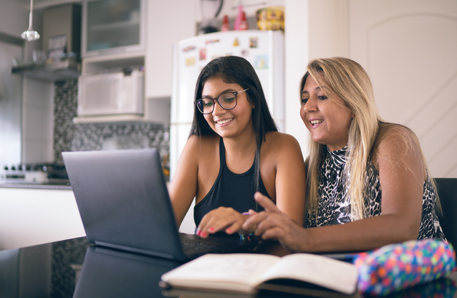 Mother and daughter sitting at table looking at laptop