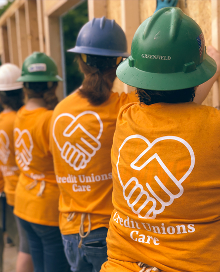 Team members building a house with shirts that say Credit Unions Care